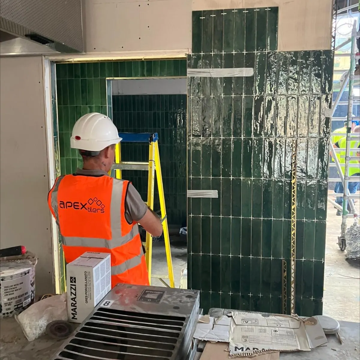 Apex Tilers fitter installing dark green metro wall tiles in a commercial kitchen fit-out