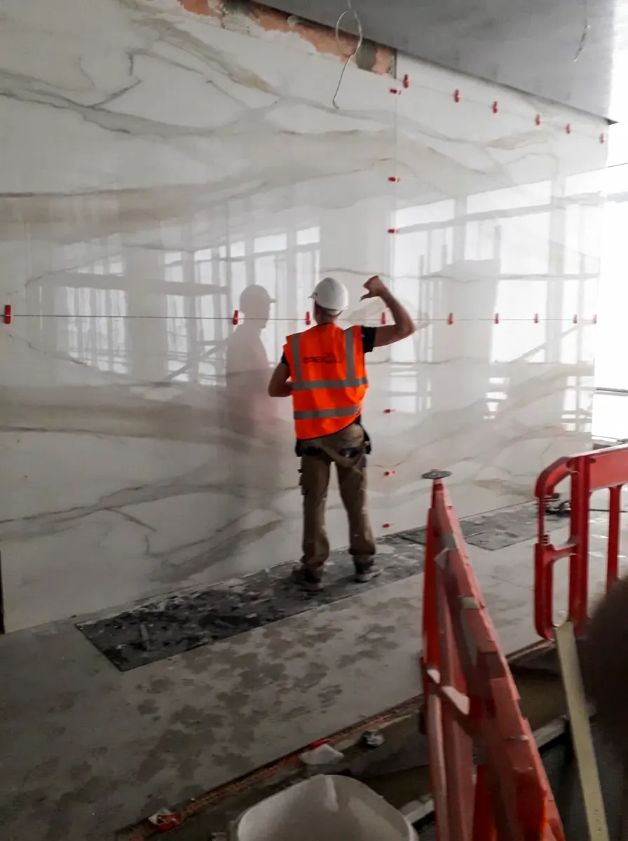 Apex Tilers fitter installing large-format marble-effect porcelain wall cladding with levelling clips on a London commercial fit-out